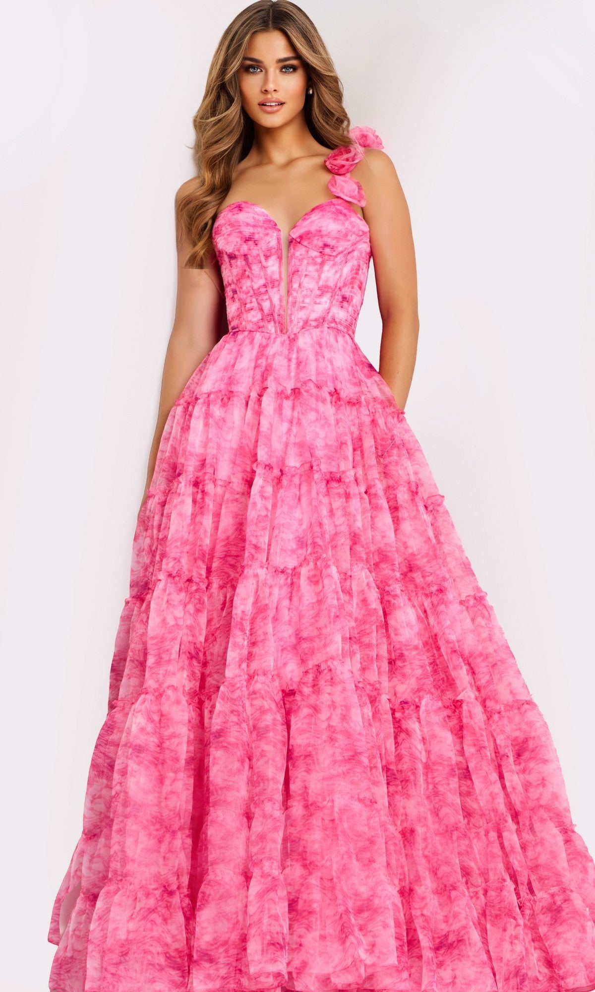 A woman stands against a plain light background wearing the Jovani 49074 long prom dress in print, featuring a floor-length skirt, fitted corset-style bodice, and floral detail on one shoulder.